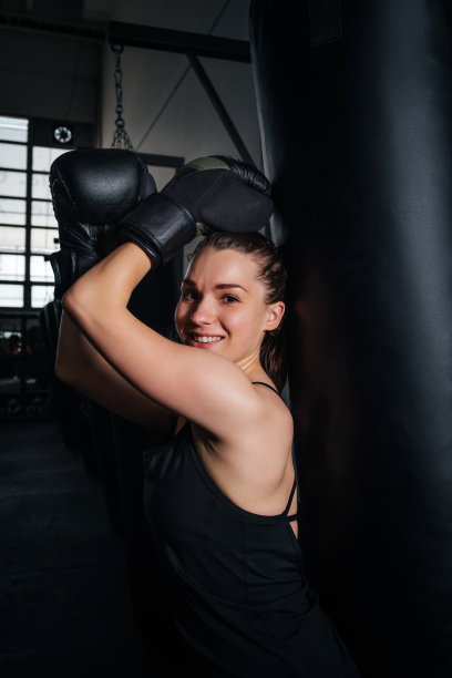 自卫。在健身房用拳击袋进行高强度锻炼。拳击女在黑暗的背景下用拳击袋摆姿势。跆拳道。性感的女孩在健身房里练习拳击。图片下载