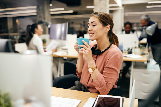 年轻的女商人在办公室休息时享受着新鲜咖啡的香味。图片下载