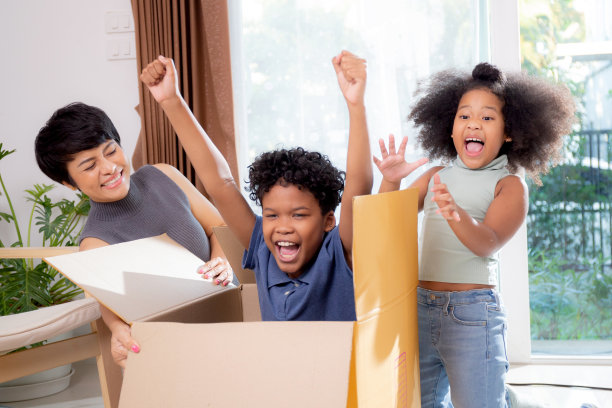 非洲家庭温馨一刻：母亲和女儿推着纸箱，儿子在客厅里兴奋地玩耍，享受家庭乐趣图片下载