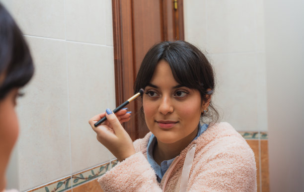 年轻女子在镜子前用刷子化妆。图片下载