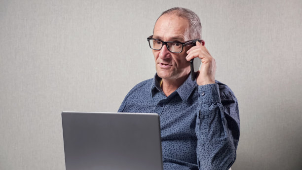 老人在桌子上用手提电脑打电话图片下载