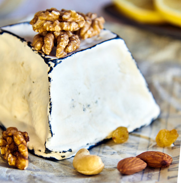 奶酪在白色的模具和黑色的木炭边缘，坚果和葡萄干，在包装纸上。图片下载