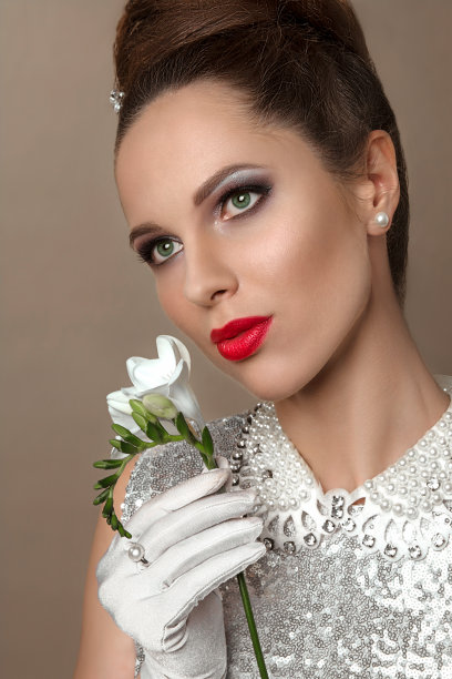 一个美丽的年轻黑发女人的肖像在一个白色闪亮的连衣裙和白色的手套与白色的花。图片下载