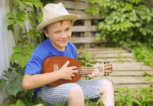 男孩玩尤克里里琴。乐器。夏天的季节。男孩的帽子。图片下载