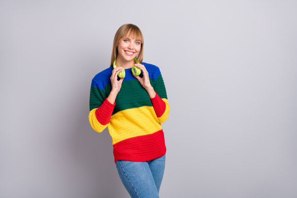 照片肖像漂亮的女人穿彩色毛衣触摸耳机孤立在柔和的灰色颜色背景图片下载