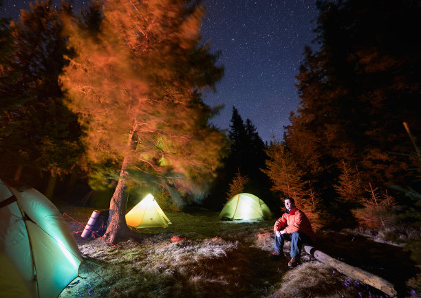 男性背包客在夜晚的原木旁休息图片下载