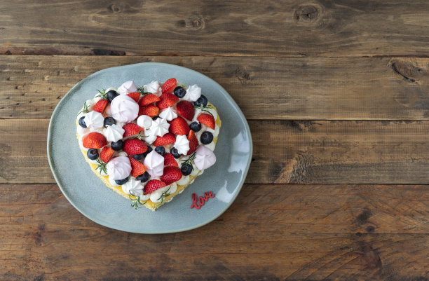 用红色水果和蛋白酥装饰的心形蛋糕。木制背景。情人节。副本的空间。图片下载