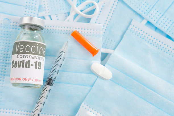 这是一张带有无菌注射器的小瓶疫苗、抗冠状病毒药物片和许多医用口罩的照片。图片下载