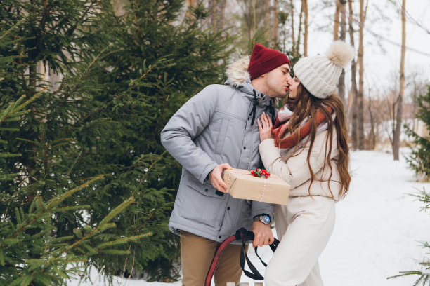 在冬天的针叶林里，情侣们拥抱亲吻，给对方装礼物的盒子图片下载