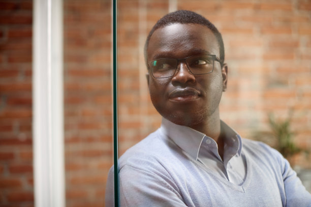 沉思的非裔美国商人站在办公室里，看着别处。图片下载