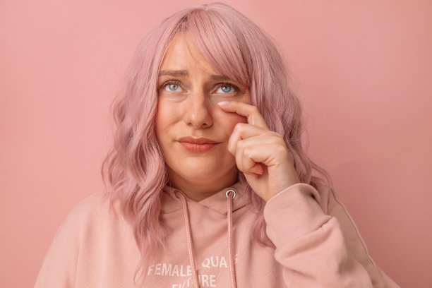 伤心不快乐的女人用粉红色的头发擦眼泪，擦她的眼泪孤立的粉红色背景抱怨着什么图片下载