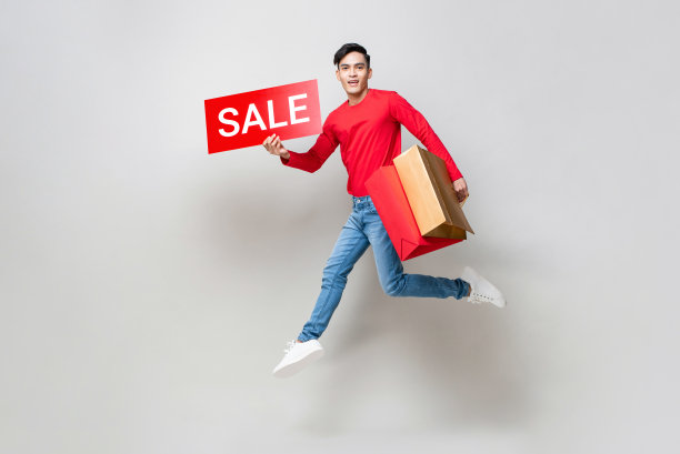 年轻的亚洲人拿着购物袋和红色的销售标志跳跃在孤立的浅灰色工作室背景中国新年销售概念图片下载
