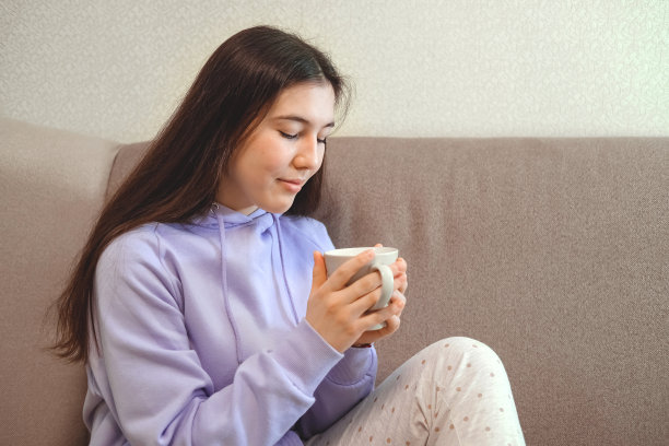 沉思的少女在家中沙发上手捧茶杯图片下载