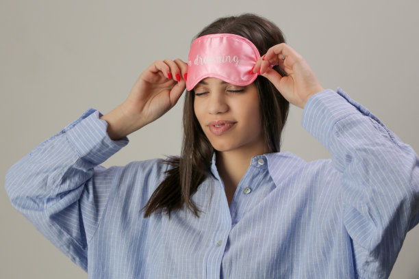 漂亮的年轻女人穿着蓝色衬衫睡衣和粉色睡眠面具的工作室肖像图片下载