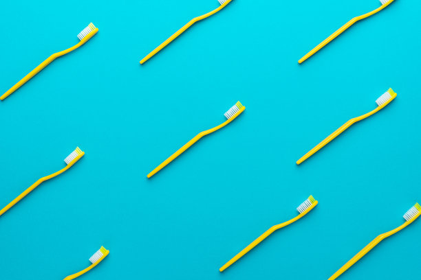 许多新的黄色塑料牙刷在蓝绿色背景的俯视图图片下载