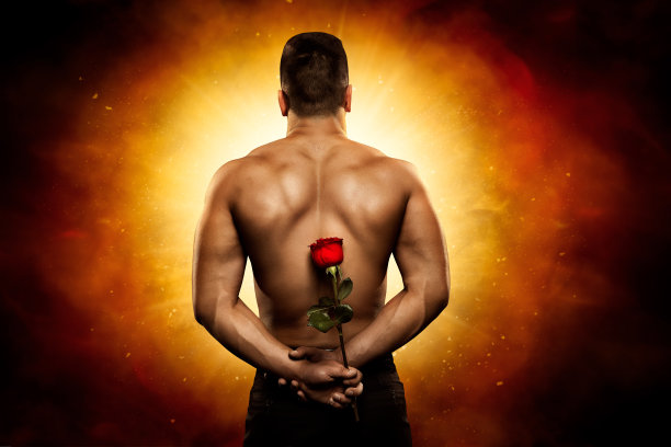 一名男子背对着神秘的闪光，将鲜花礼物藏在背后。强壮的肌肉上身裸露健美者背后与红玫瑰在艺术幻想背景图片下载
