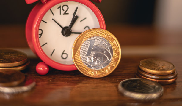 雷亚尔-巴西雷亚尔，巴西货币。照片聚焦在一枚真正的硬币旁边的一个红色的钟在一个住宅的窗口。储蓄，投资，退出，未来计划的概念。图片下载