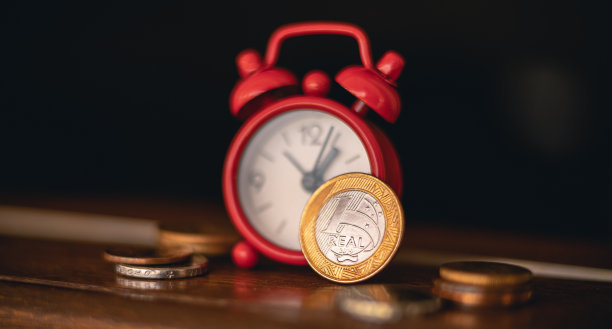 雷亚尔-巴西雷亚尔，巴西货币。照片聚焦在一枚真正的硬币旁边的一个红色的钟在一个住宅的窗口。储蓄，投资，退出，未来计划的概念。图片下载