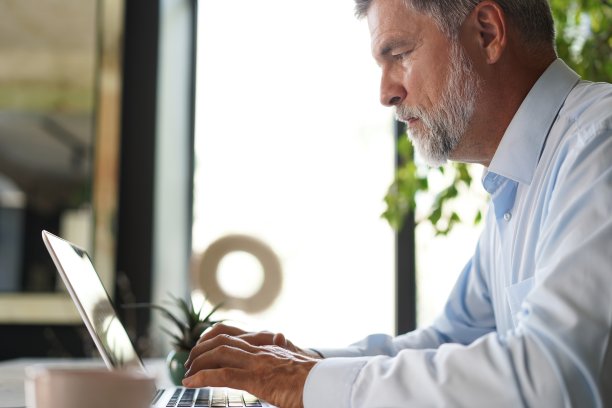 灰色头发的高级男子在办公室用笔记本电脑工作的肖像。图片下载