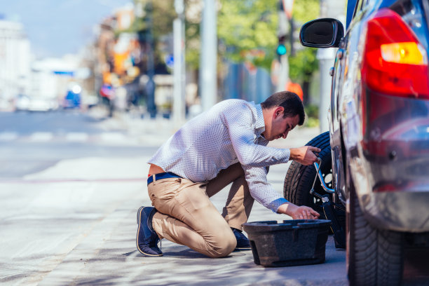 一个强壮的商人正弯着膝盖，试图用他的扳手换掉他车上的一个平头。图片下载