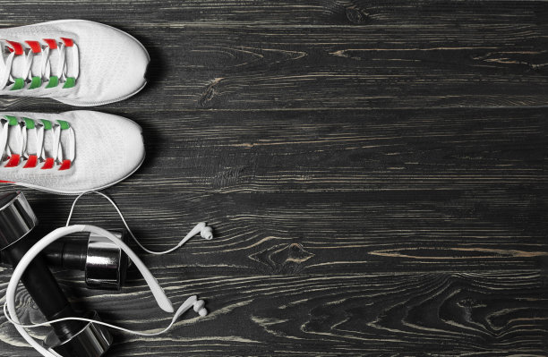 训练用的白色运动鞋，黑色木质背景的哑铃和耳机。图片下载