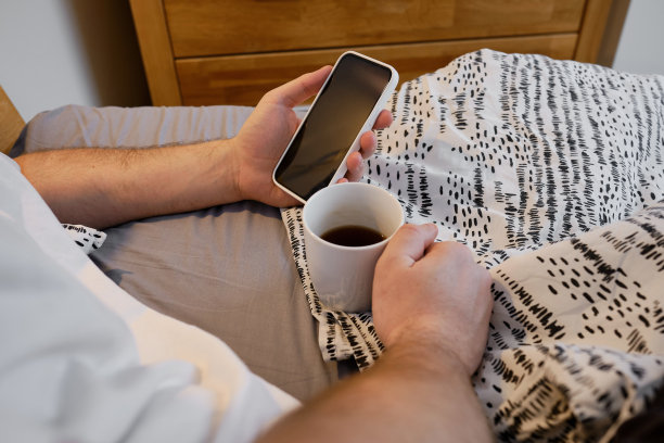 男人在床上拿着智能手机，在睡觉前或起床后查看社交网络账户。小玩意上瘾。一个男人在用手机发短信图片下载