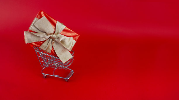红色背景的购物车里有金色蝴蝶结的礼物。图片下载