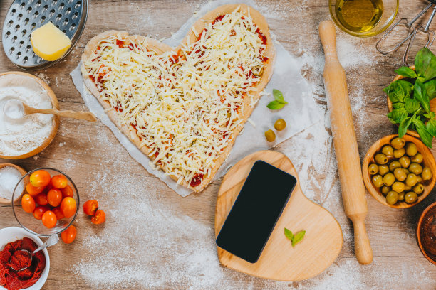 智能手机旁边的心形自制披萨图片下载