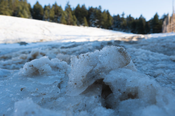 肮脏的冰部分在积雪的道路和模糊的森林背景在冬天图片下载