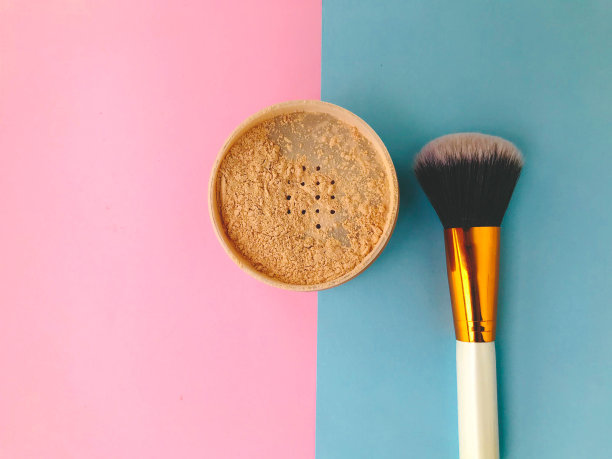 在明亮的背景上涂抹松散的粉末。在粉妆刷旁边。粉末刷，蓬松，由天然材料制成。白柄金头刷图片下载