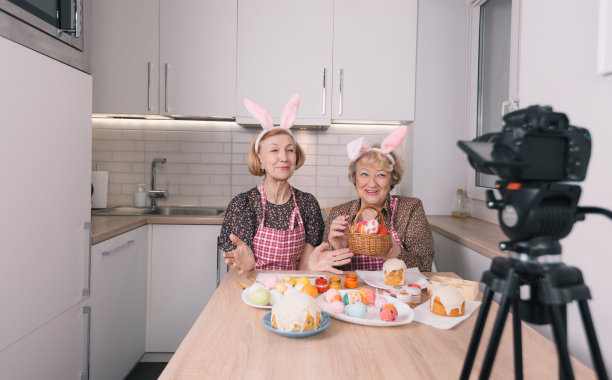 两名头上戴着兔耳朵的老年妇女看着摄像机拍摄视频博客。为复活节假期做准备图片下载