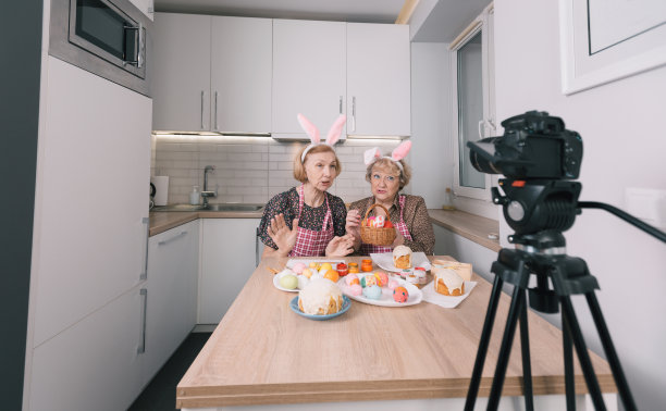 两名头上戴着兔耳朵的老年妇女看着摄像机拍摄视频博客。为复活节假期做准备图片下载