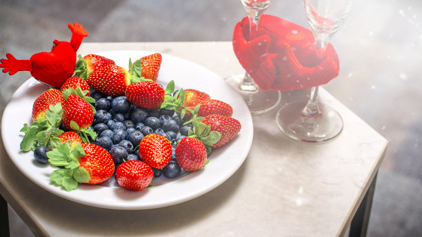情人节的背景，一盘草莓和蓝莓，桌子上有两个香槟杯。图片下载