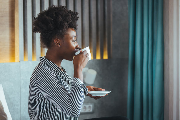 年轻漂亮的黑人女人，卷着头发，穿着白色条纹衬衫，在酒店喝咖啡图片下载