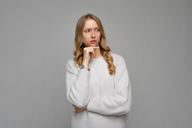有思想的漂亮女人，金发，神情沉思，计划着即将到来的周末，穿着白色的毛衣，灰色的背景。困惑的女性图片下载