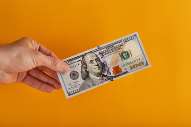 手里拿着一张百元美钞，背景是黄色/橙色图片下载