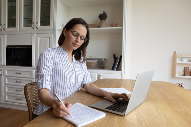 专注的千禧一代女学生戴着眼镜，在笔记本电脑上写笔记图片下载