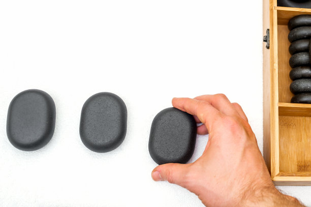 热的石头按摩在一个木制的盒子旁边的石头在按摩师的手孤立在白色背景顶视图。图片下载