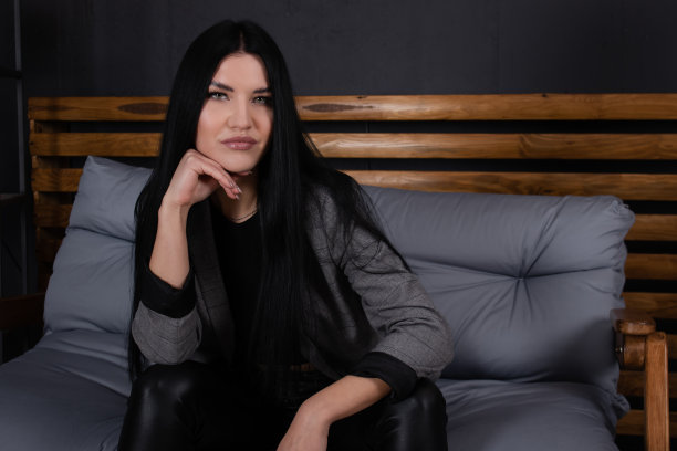 自信的黑发女人在灰色的阁楼房间黑色坐在沙发上。时髦的衣服。时尚女性肖像图片下载