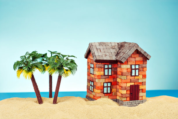 在沙滩上模拟一座房子。以大海和蓝天为背景的海滨别墅。买房和抵押贷款的概念。房子附近有棕榈树和天堂岛。图片下载