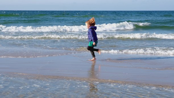 年轻快乐的白人女孩在绿色的裙子在阳光明媚的大风天赤足沿着海滩跑图片下载
