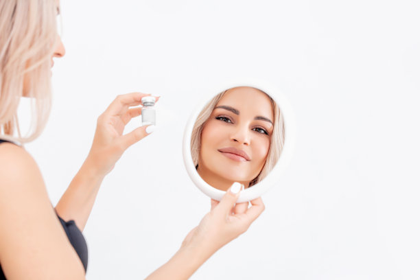 一个美丽的金发女郎的肖像在镜子的反射与自然化妆在白色的背景。影棚拍摄。图片下载