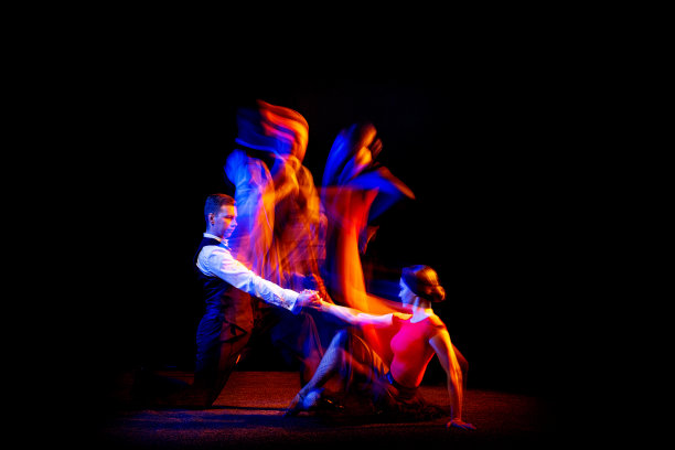 年轻的交际舞舞者跳舞的阿根廷探戈的动态肖像孤立在黑暗的背景与霓虹灯混合光。图片下载