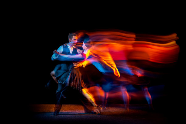 年轻的交际舞舞者跳舞的阿根廷探戈的动态肖像孤立在黑暗的背景与霓虹灯混合光。图片下载