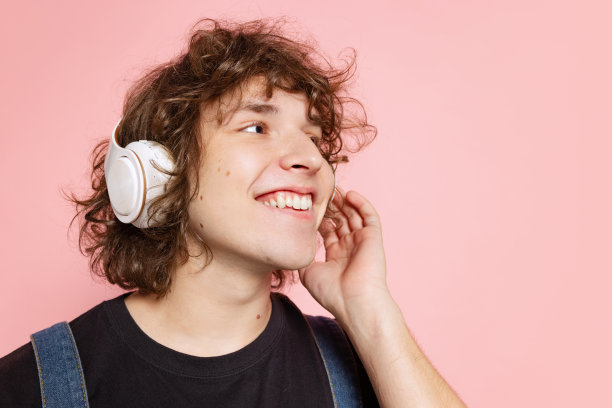 特写年轻英俊的男子，学生穿着黑色t恤，戴着耳机在粉红色的背景下。情感的概念图片下载