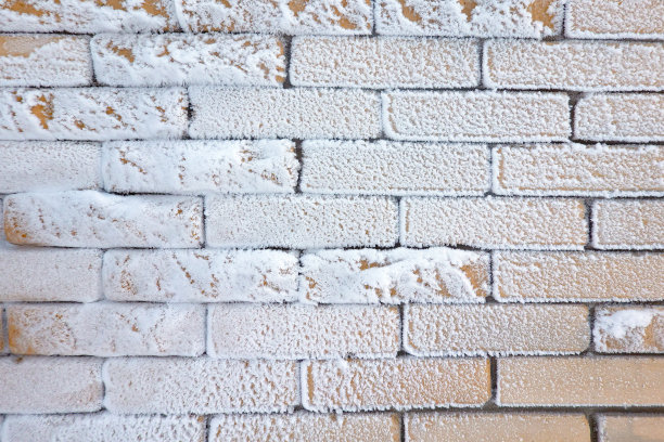 黄色的砖墙上覆盖着在寒冷中形成的雪和冰晶。背景。纹理。图片下载