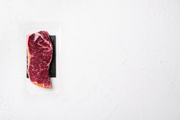 新鲜的肉，真空包装的大理石牛肉，纽约条形牛排，在白色石头桌子背景，俯视图平躺，与文本的拷贝空间图片下载