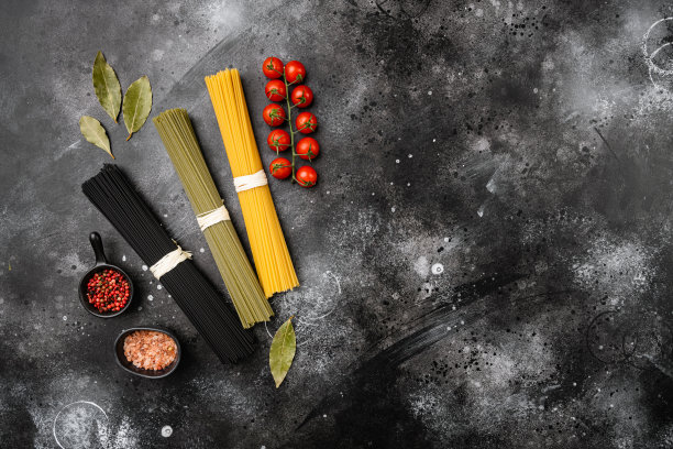 意大利面有三种颜色，黑、黄、绿，在黑、黑的石头桌子背景上，俯视图平铺，文字有复制空间图片下载