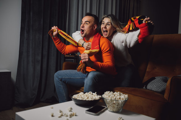 球迷拥抱着深色头发大喊大叫热情的男人和金发女人与围巾尖叫体育比赛在室内的沙发图片下载