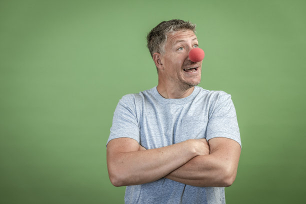 红色小丑鼻子的男人在绿色背景前面图片下载